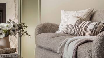A cozy living room with a sofa, a vase with flowers, and a window with a view of greenery.