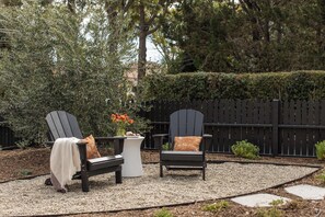 Two Adirondack chairs with cushions, a small round table with a vase of flowers, and a gravel patio area. - The Craft House Inn (Santa Barbara)