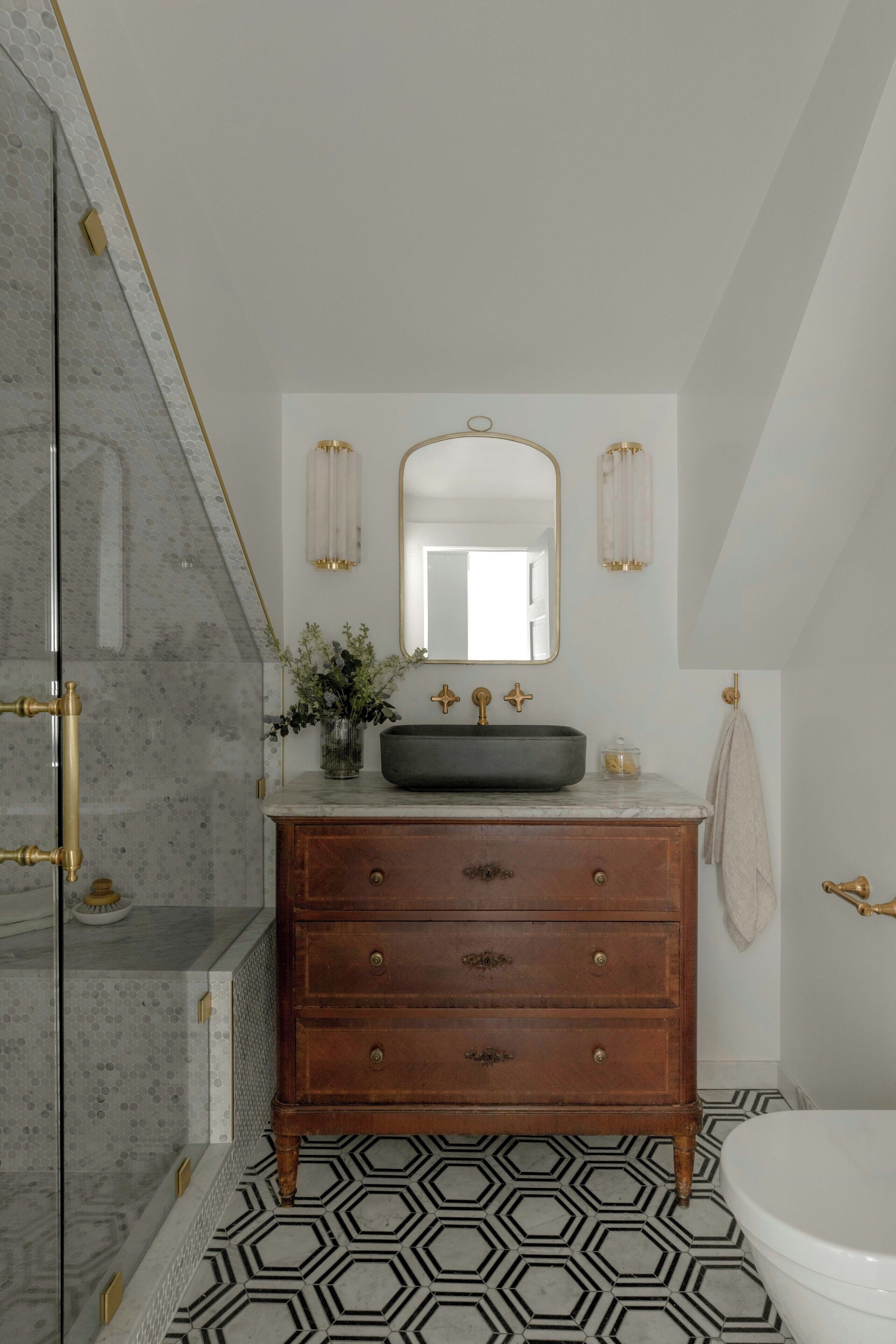 A bathroom with a marble floor, a wooden vanity with a sink, and a large mirror above it.