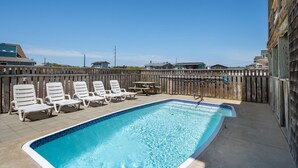A rectangular swimming pool with a tiled edge, surrounded by white lounge chairs and a wooden fence. - Footloose & Fab-Semi-oceanfront, pool, hot tub, rec room, pool table, elevator! (Nags Head)