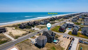 An aerial view of a coastal residential area with houses, a beach access point, and a clear view of the ocean. - Footloose & Fab-Semi-oceanfront, pool, hot tub, rec room, pool table, elevator! (Nags Head)
