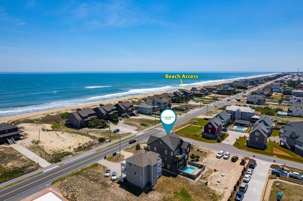An aerial view of a coastal residential area with houses, a beach access point, and a clear view of the ocean.