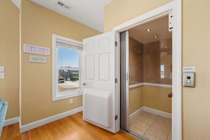 A room with a white door, a window with a view, and an elevator. - Footloose & Fab-Semi-oceanfront, pool, hot tub, rec room, pool table, elevator! (Nags Head)