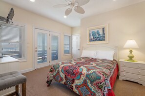 A bedroom with a large bed, a desk, a chair, a ceiling fan, and a painting on the wall.