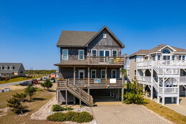 A two-story wooden building with a balcony, a staircase, and a signboard. - Footloose & Fab-Semi-oceanfront, pool, hot tub, rec room, pool table, elevator! (Nags Head)