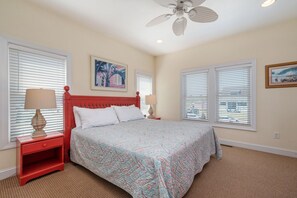 A bedroom with a bed, two nightstands, a ceiling fan, and two windows with blinds. - Footloose & Fab-Semi-oceanfront, pool, hot tub, rec room, pool table, elevator! (Nags Head)