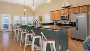 A kitchen with a central island, bar stools, wooden cabinets, a refrigerator, and a microwave. - Footloose & Fab-Semi-oceanfront, pool, hot tub, rec room, pool table, elevator! (Nags Head)