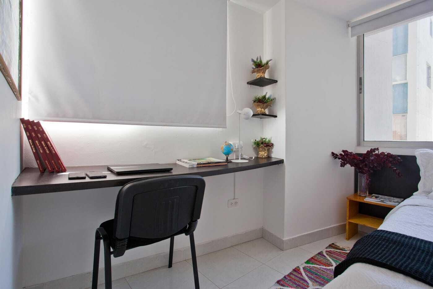 Une chambre moderne équipée d’un bureau, d’une chaise, d’un lit et d’étagères ornées de plantes.