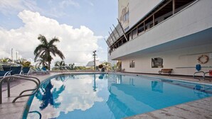 A swimming pool with lounge chairs and palm trees, surrounded by a modern building with a white facade.