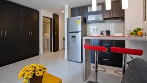 A modern kitchen with dark cabinets, a stainless steel refrigerator, a microwave, and a granite countertop. There are two red bar stools and a vase of yellow flowers on a wooden table.