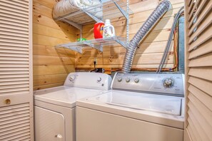 Compact laundry room with two front-loading washing machines and storage for cleaning supplies.