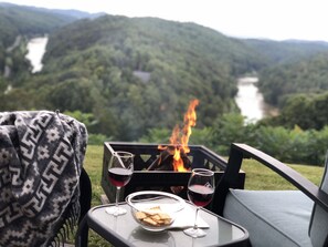 A table with a glass of red wine, a bowl of crackers, and a fire pit with flames.