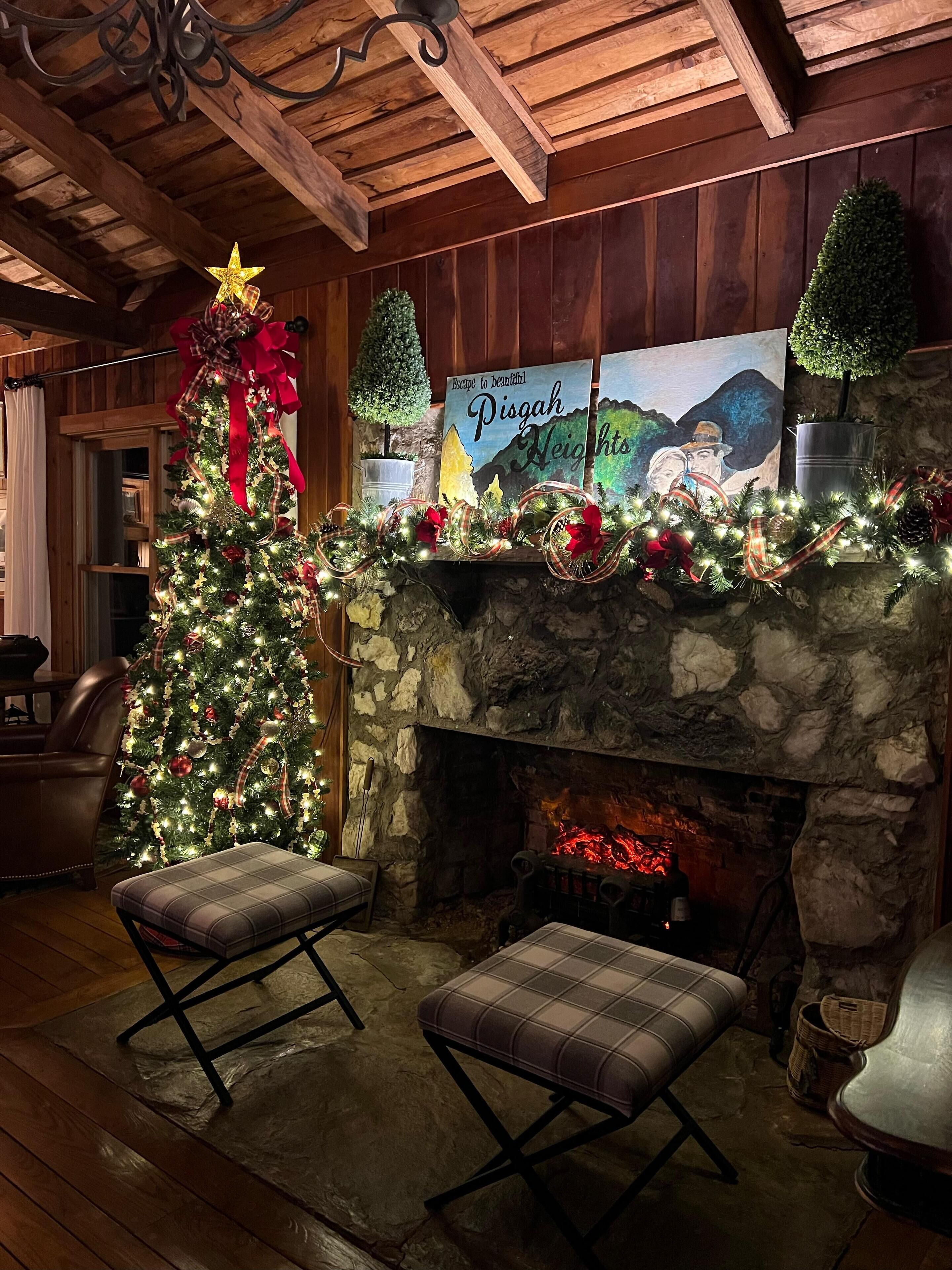 Un cuarto acogedor con chimenea de piedra, un árbol de Navidad y un cuadro titulado 'Escape to Beautiful Pisgah Heights'.