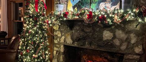 Un cuarto acogedor con chimenea de piedra, un árbol de Navidad y un cuadro titulado 'Escape to Beautiful Pisgah Heights'.