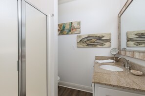Ein Badezimmer mit weißer Tür, Waschbecken mit Granitplatte, Spiegel und zwei Wandbildern.