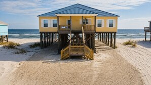 Een strandhuis met een blauw dak, houten terras en een trap naar de ingang.