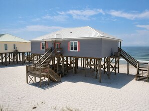 A beach house with a staircase leading to a deck, a pool, and a view of the ocean.