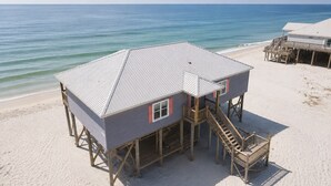 Une maison de plage avec un toit en métal, une terrasse en bois et un escalier menant à l’entrée principale.