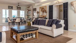 A spacious living room with a white sofa, a wooden coffee table, and a dining area with chairs and a table.