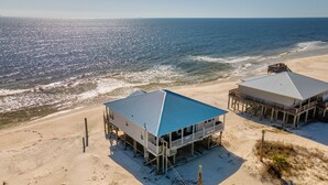 A beachfront property with two buildings, one with a blue roof and another with a grey roof, both elevated on stilts.