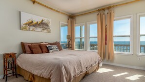 A bedroom with a large bed, a view of the sea, and a painting of birds.