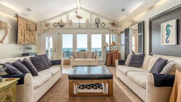 A spacious living room with two white sofas, a wooden coffee table, and a view of the sea through large windows.