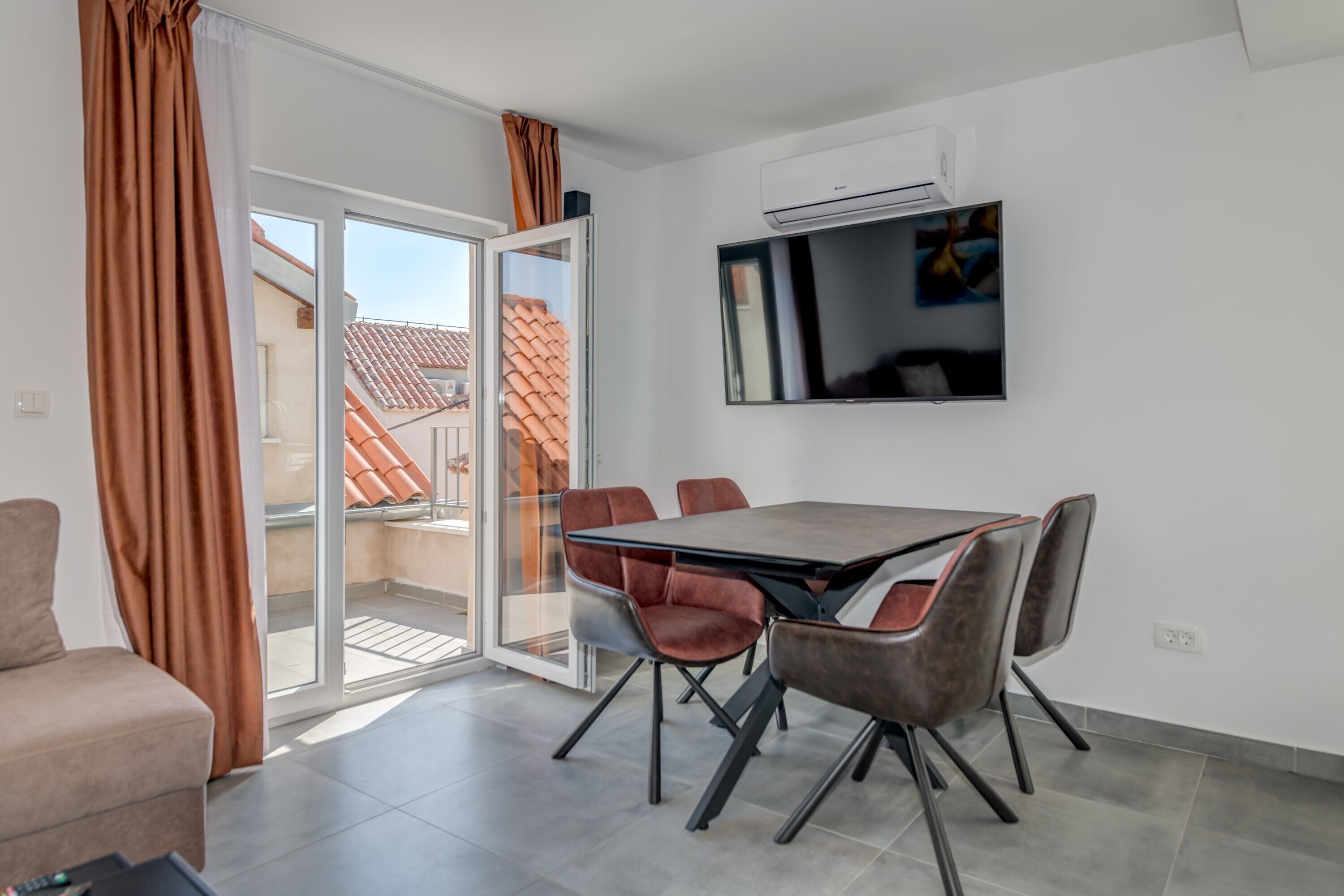 A modern living room with a dining area, a sliding glass door to a balcony, and a mounted TV.
