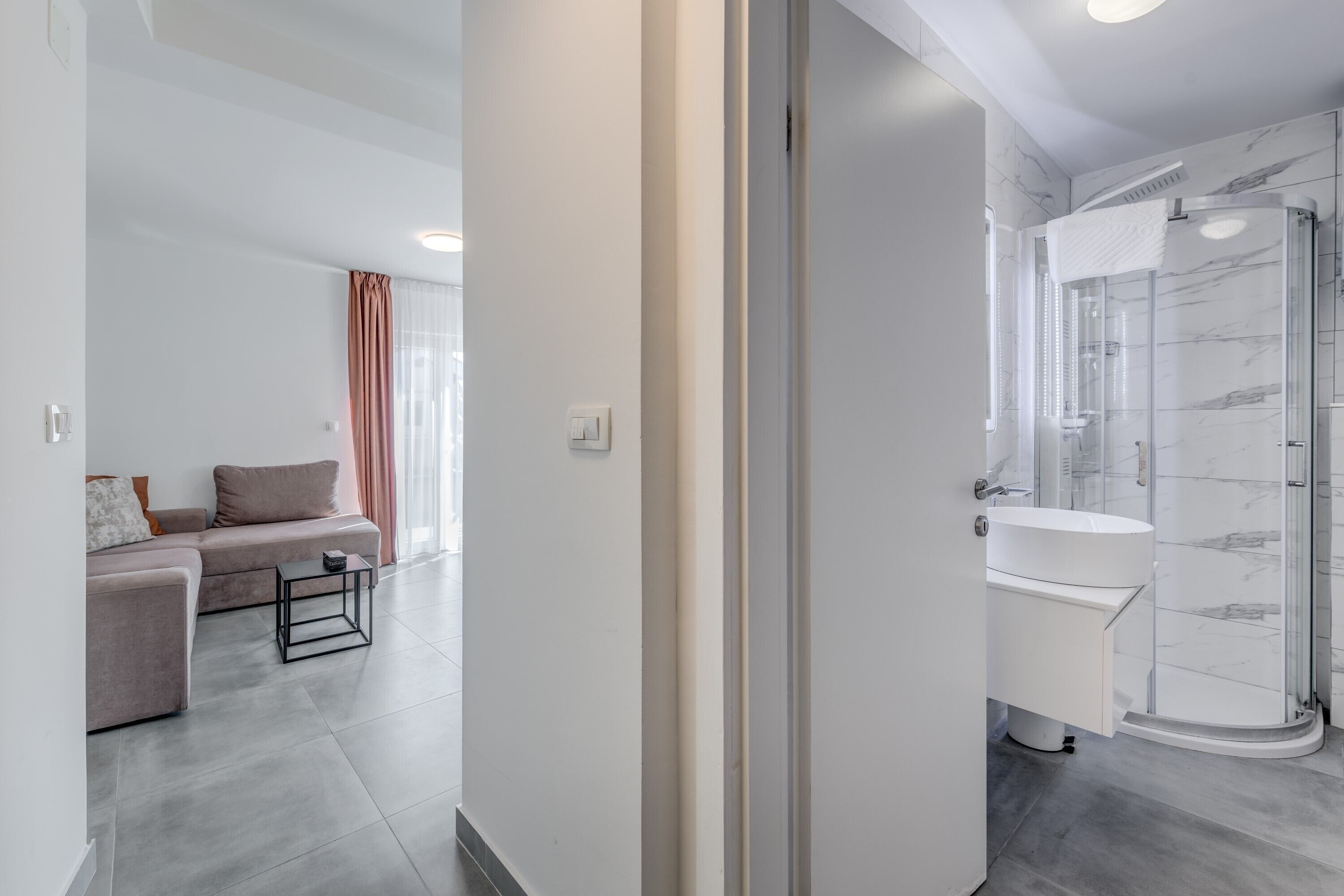 A modern bathroom with a glass shower enclosure, a white sink, and a marble backsplash.