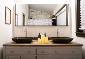 Un baño con lavamanos doble, dos velas y un espejo grande sobre el tocador.