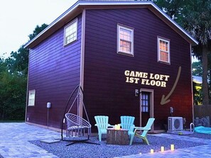 Un edificio con un cartel que dice 'GAME LOFT PRIMER PISO' y área de estar exterior con sillas y una mesa.