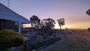 Een woonhuis met een overdekt terras, gazon en diverse beplanting.