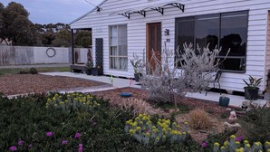 Een wit huis met een veranda, grote ramen en een tuin vol planten en bloemen.