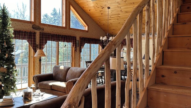 A wooden interior with a staircase, large windows, and a Christmas tree.