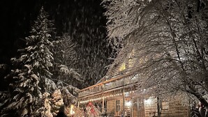 A log cabin with a snow-covered exterior and a lit porch.