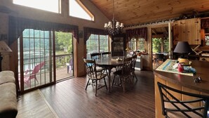 A spacious room with a large dining table, wooden flooring, and a view through large windows.