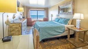 Una habitació d'hotel amb un llit, dues cadires, un escriptori, una làmpada i vista a l'oceà.