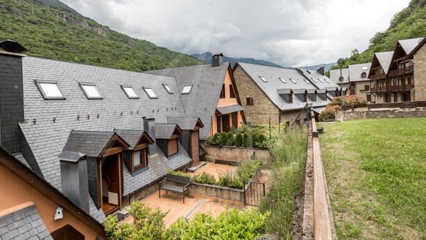 A residential area with multiple houses featuring sloped roofs and skylights, surrounded by lush greenery and hills in the background. - Casa Artiga de Lin (Bòrdes (Es))