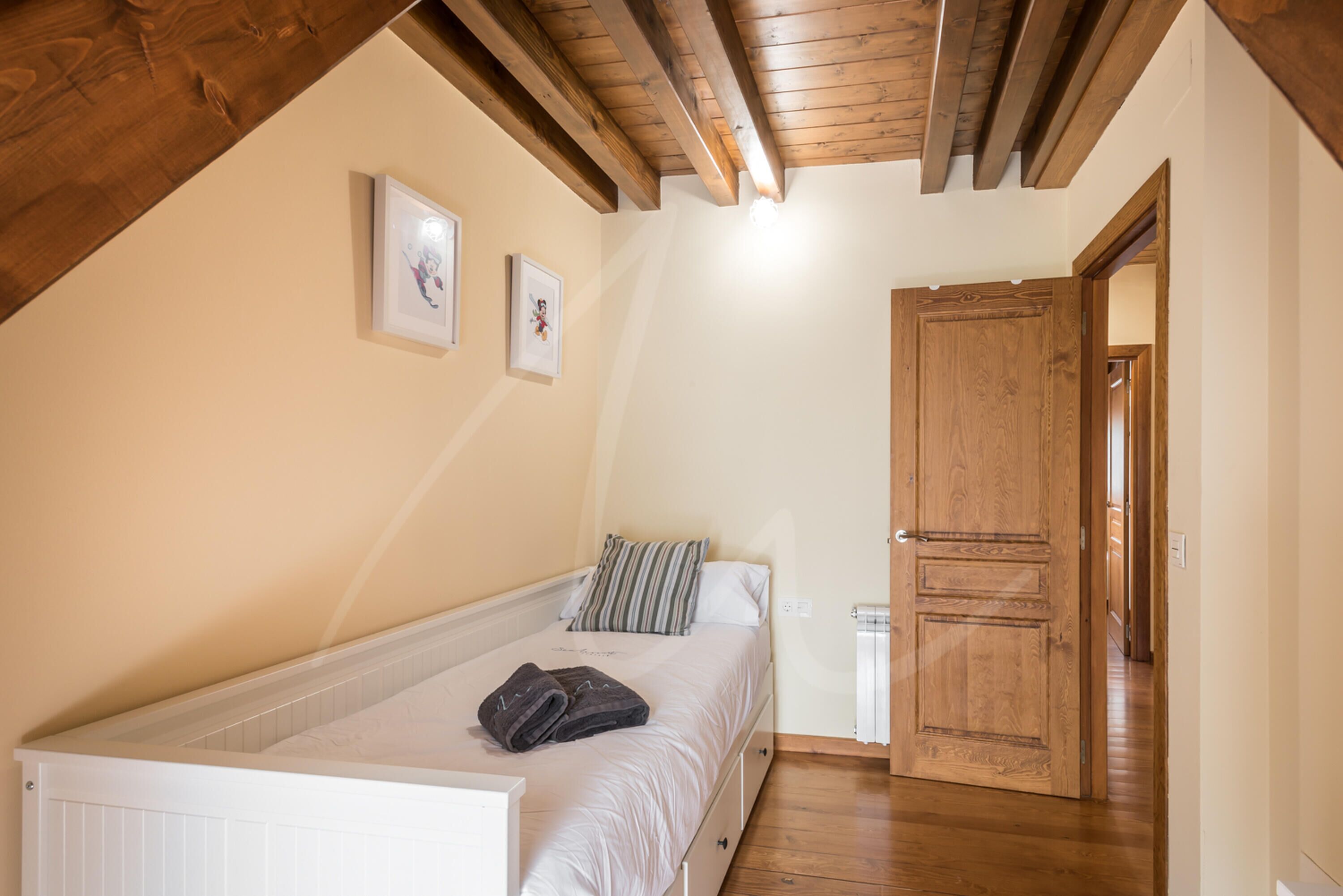 Une chambre à coucher avec un lit, des poutres en bois au plafond, une porte et un radiateur.