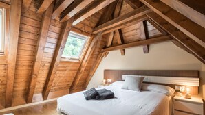 A bedroom with a sloped ceiling, wooden beams, a large bed, bedside tables, and a window. - Casa Artiga de Lin (Bòrdes (Es))