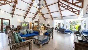 A spacious living area with a high ceiling, wooden beams, and a central seating area with sofas and a coffee table.