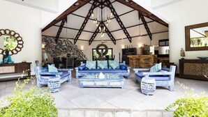 A spacious indoor area with a high ceiling, wooden beams, and a central seating arrangement with blue upholstered sofas and a coffee table.
