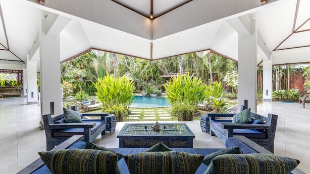 A modern indoor space with a pool, seating area, and lush greenery visible through large windows.
