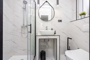 Un baño moderno con ducha envuelta en vidrio, un lavamanos blanco y un espejo redondo.