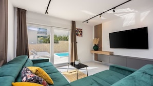 Un salón moderno con un sofá grande color verde, un televisor de pantalla plana y vista a una piscina a través de puertas de vidrio.