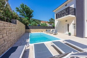 Una piscina con sillas de descanso, un muro de piedra y un edificio con balcón.