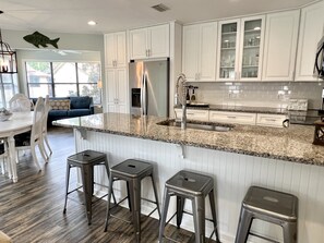 A modern kitchen with white cabinets, a granite countertop, stainless steel appliances, and a large island with stools. - Bright, newly updated 3 BR 2 BA condo - Walk to Pier and Village! (St. Simons Island)