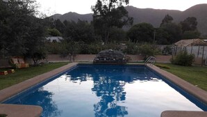 Ein rechteckiger Swimmingpool mit klarem, blauem Wasser, umgeben von einer Betonplattform und einem Steinbau in der Mitte.