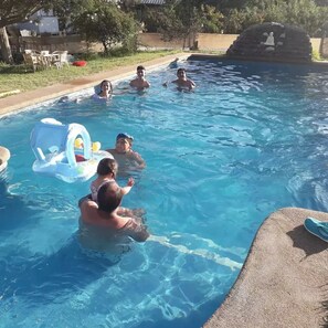 A swimming pool with clear blue water, a floating toy, and a stone sculpture.