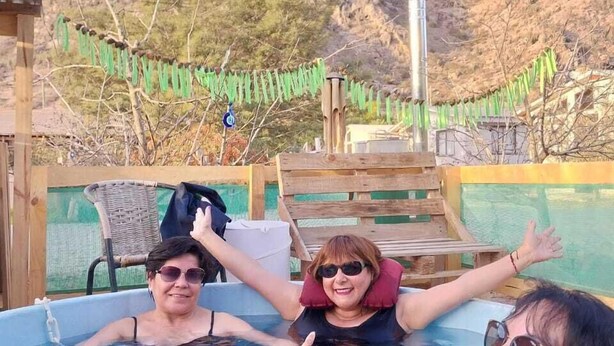 Ein Whirlpool mit zwei Personen, umgeben von einer Holzterrasse und einem Bergpanorama.