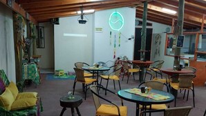 Ein gemütlicher Innenraum mit Holzbalken, runden Tischen mit gelben Kissen und einem Neonzeichen an der Wand.